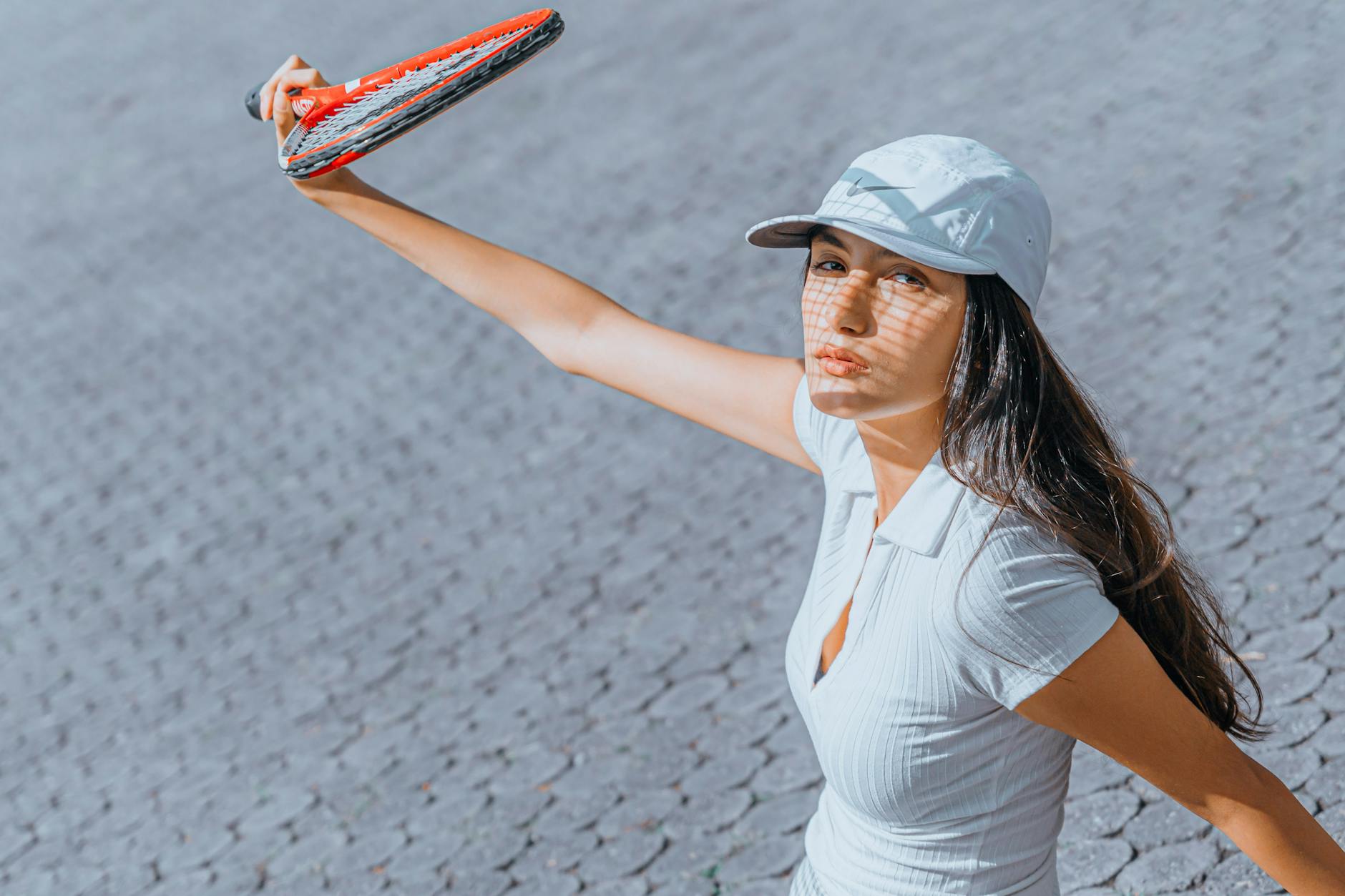 Woman wearing white cap and dress holding a tennis racket on a sunny day.