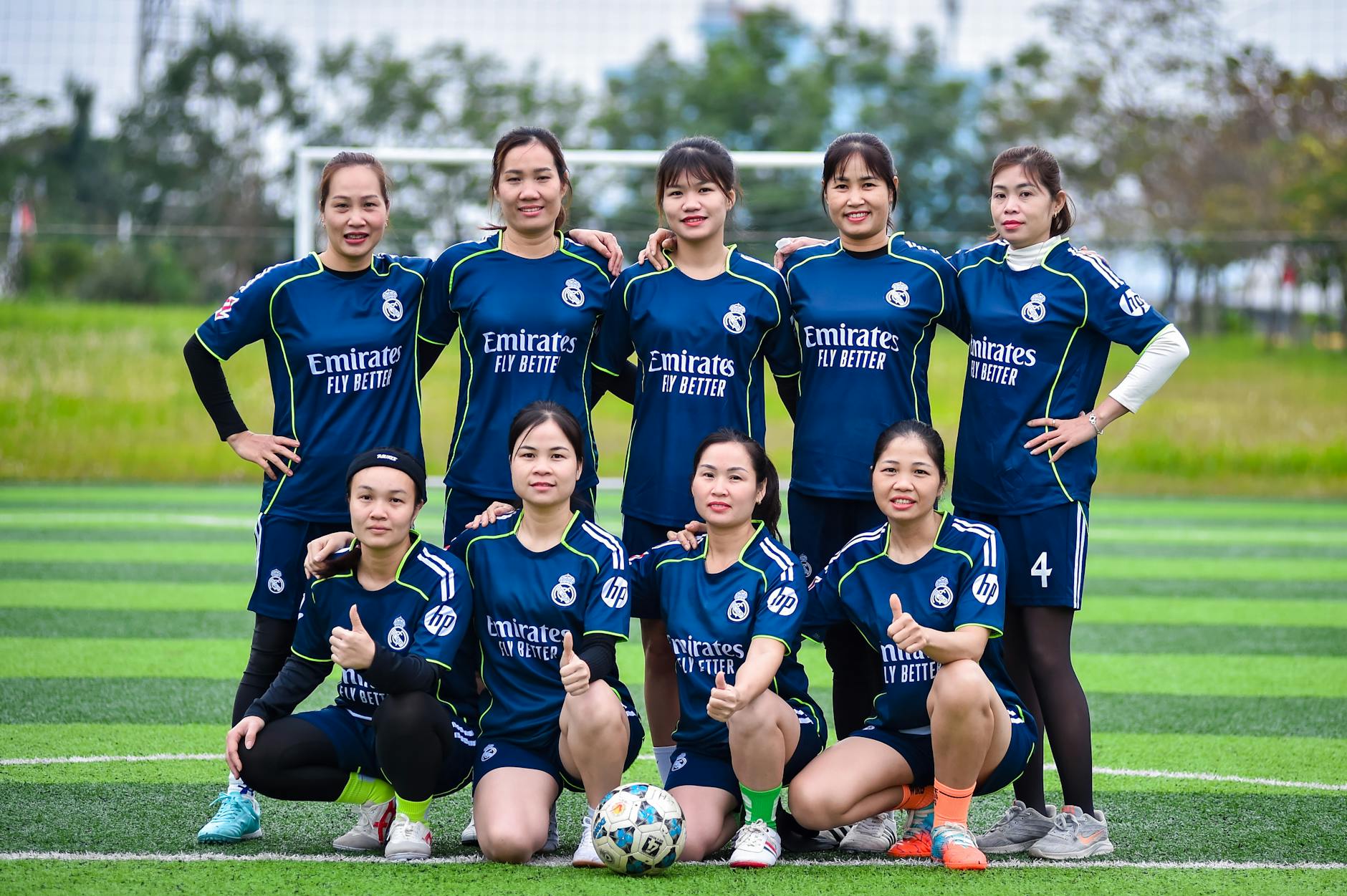 A women's football team poses for a group photo on a green field in Hanoi, Vietnam.