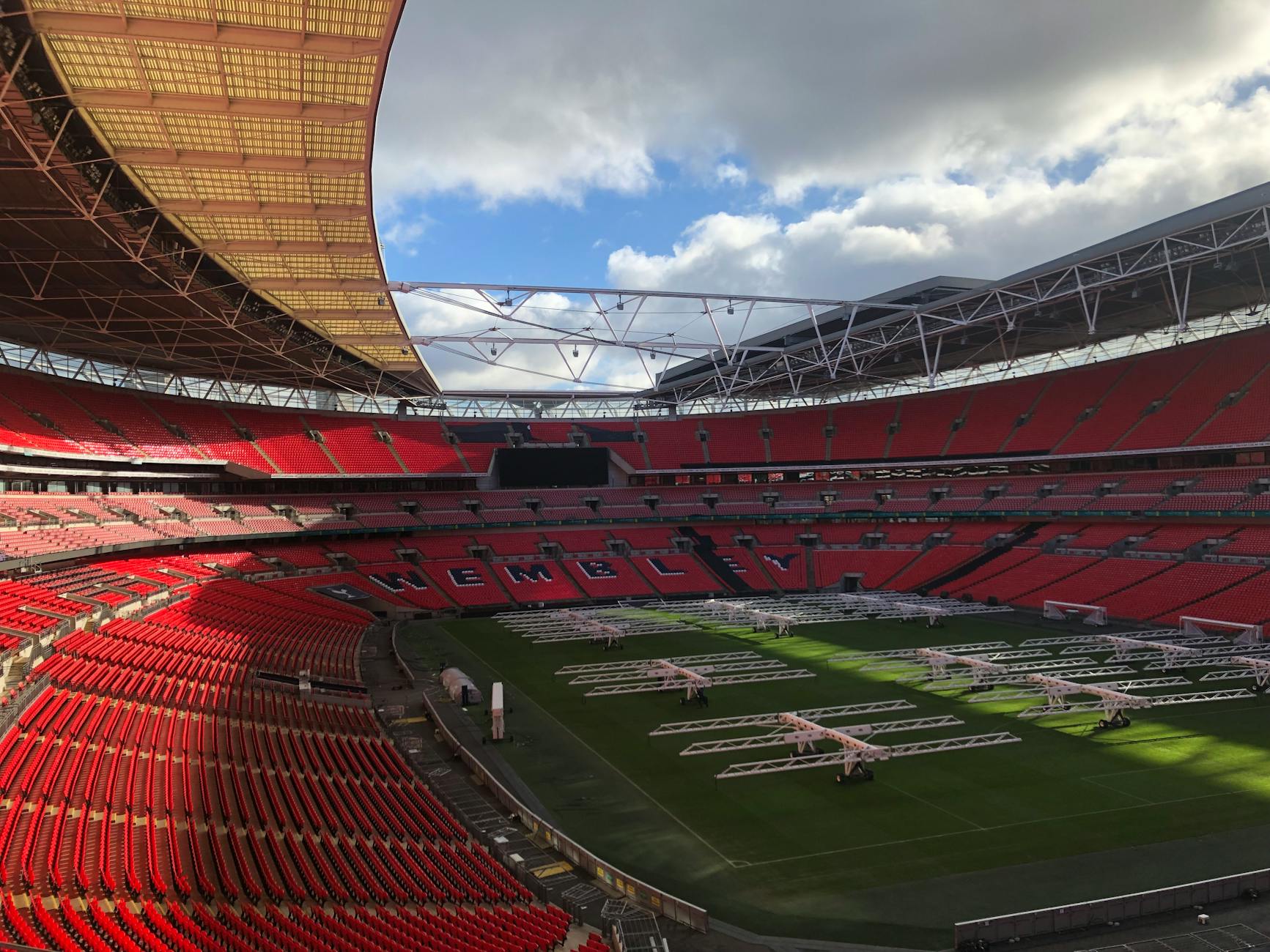 A view of an empty Wembley Stadium under a dramatic sky, showcasing its iconic architecture and red seats.