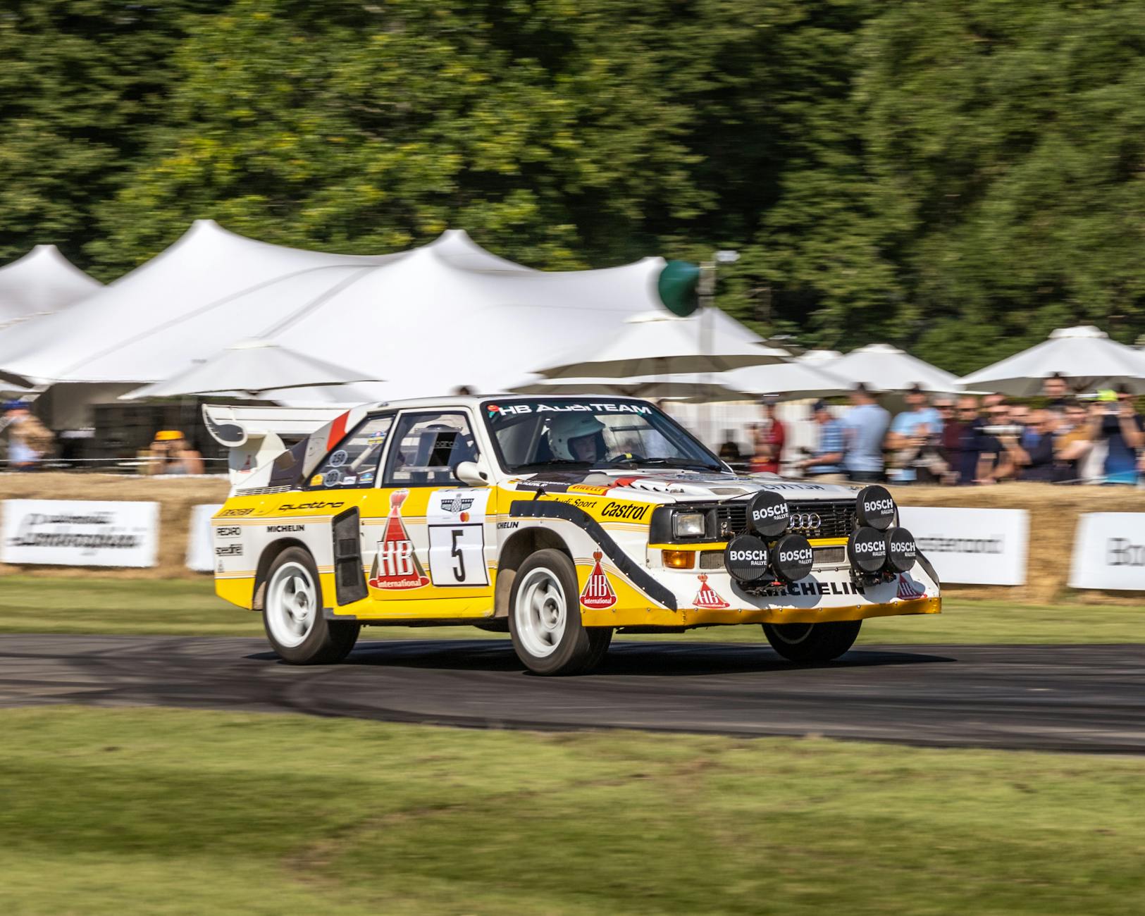 An Audi rally car speeds around a track at an outdoor event in England.