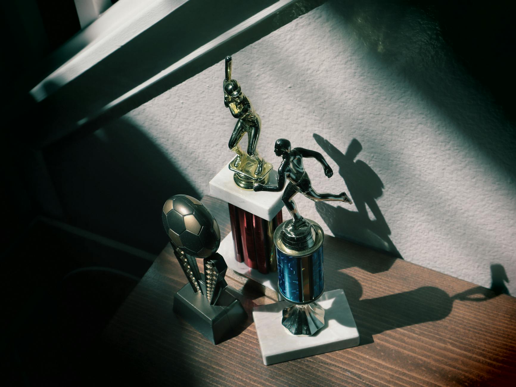 Collection of baseball and soccer trophies in sunlight, highlighting childhood achievements.