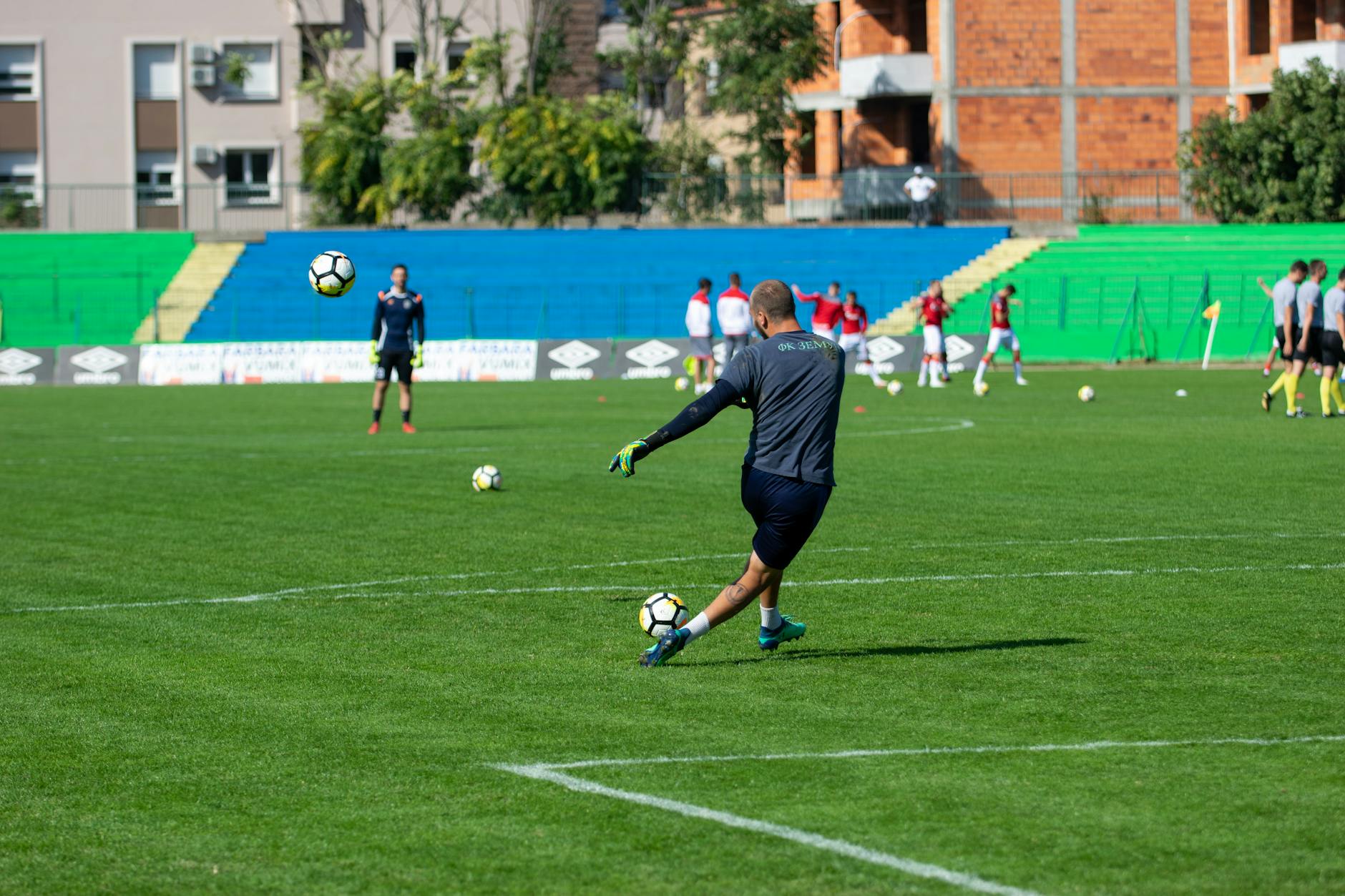 Soccer player kicking a ball during training on a green field under sunny skies.