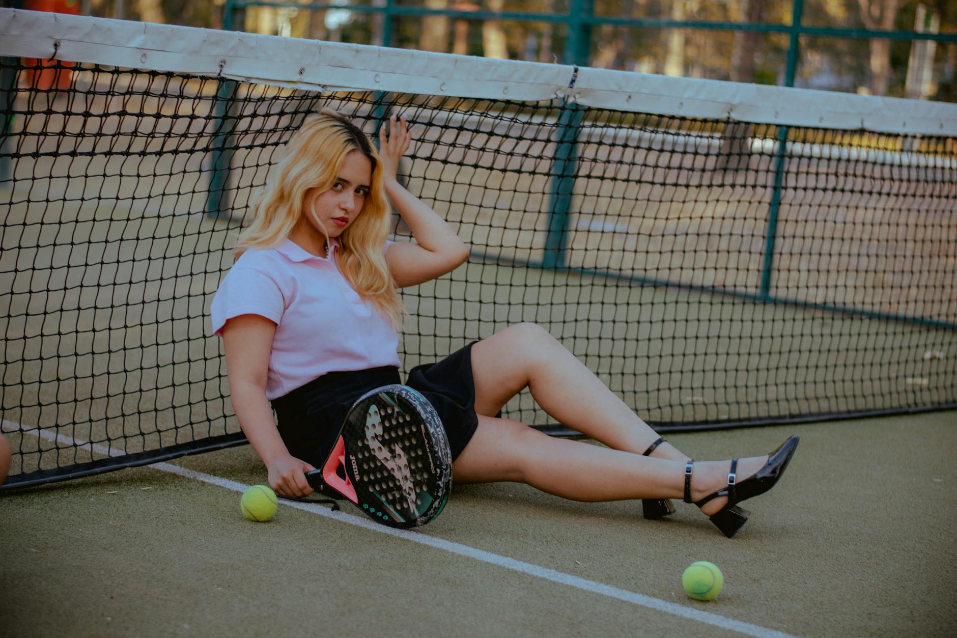 Stylish young woman posing by tennis net with racket on outdoor court.