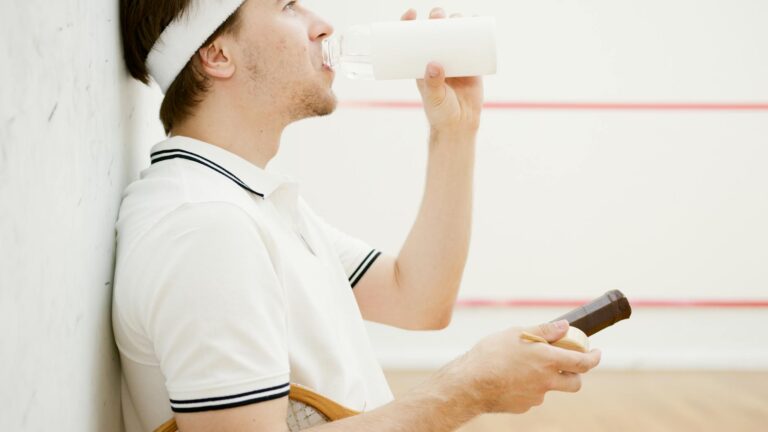 Caucasian man in sportswear resting and drinking water after a squash game.