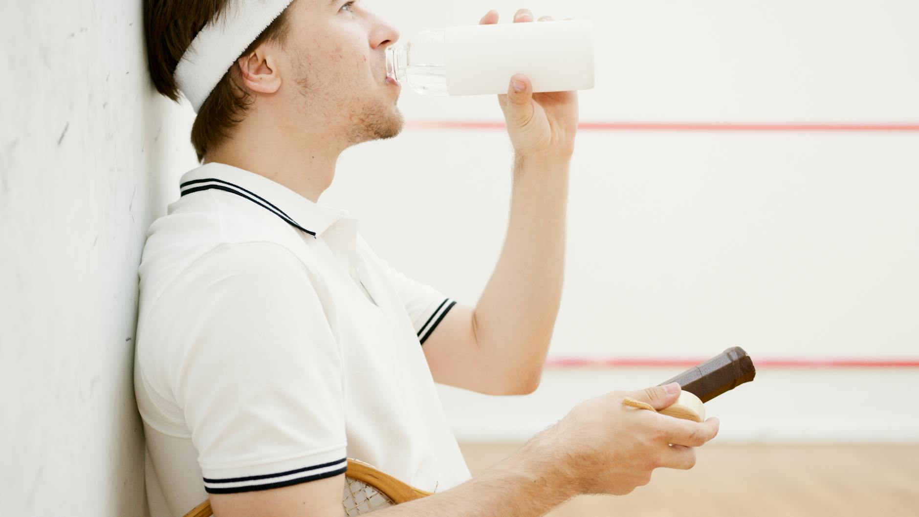 Caucasian man in sportswear resting and drinking water after a squash game.