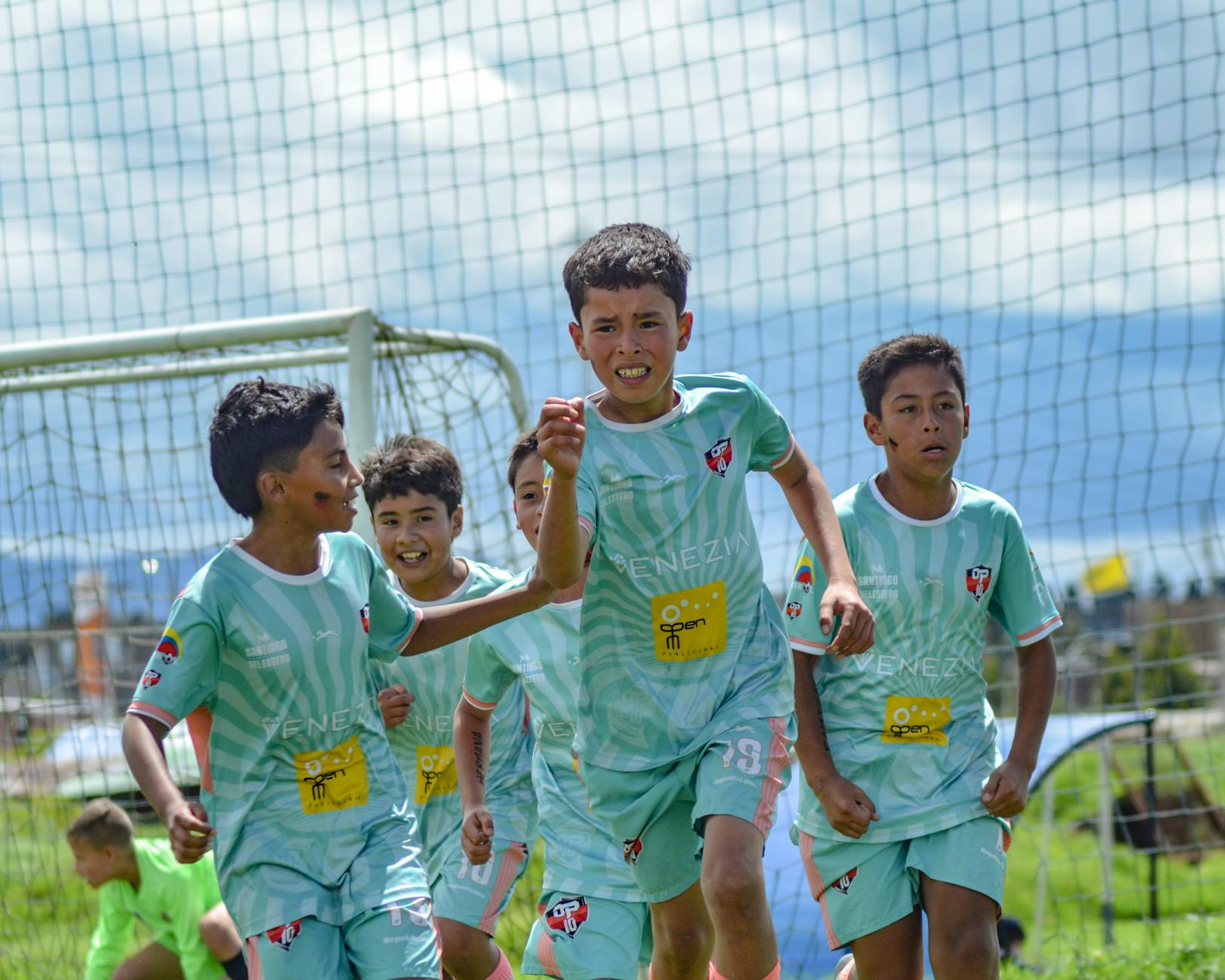 Energetic young soccer players celebrating a goal on a sunny day.