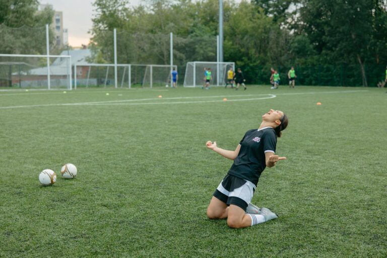 Female soccer player celebrating with arms raised on outdoor field.
