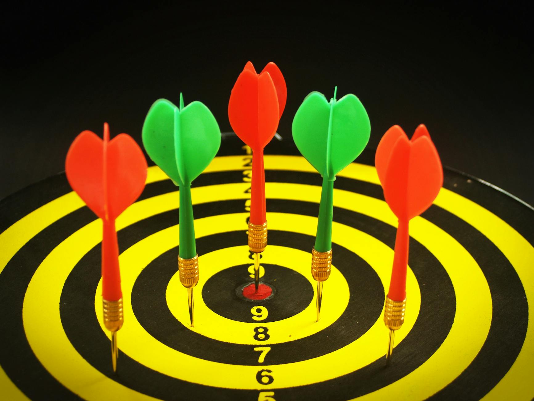 A close-up of colorful darts hitting the bullseye on a yellow and black dartboard.