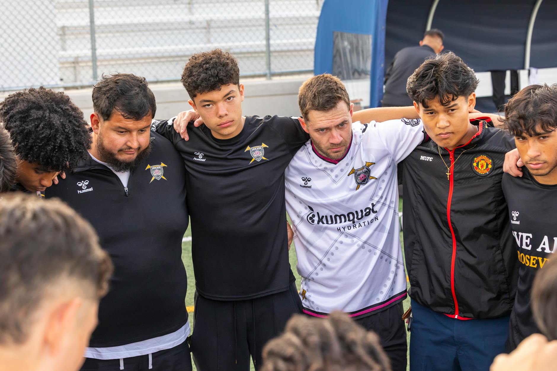 A soccer team group huddle shows unity and teamwork on an outdoor field.