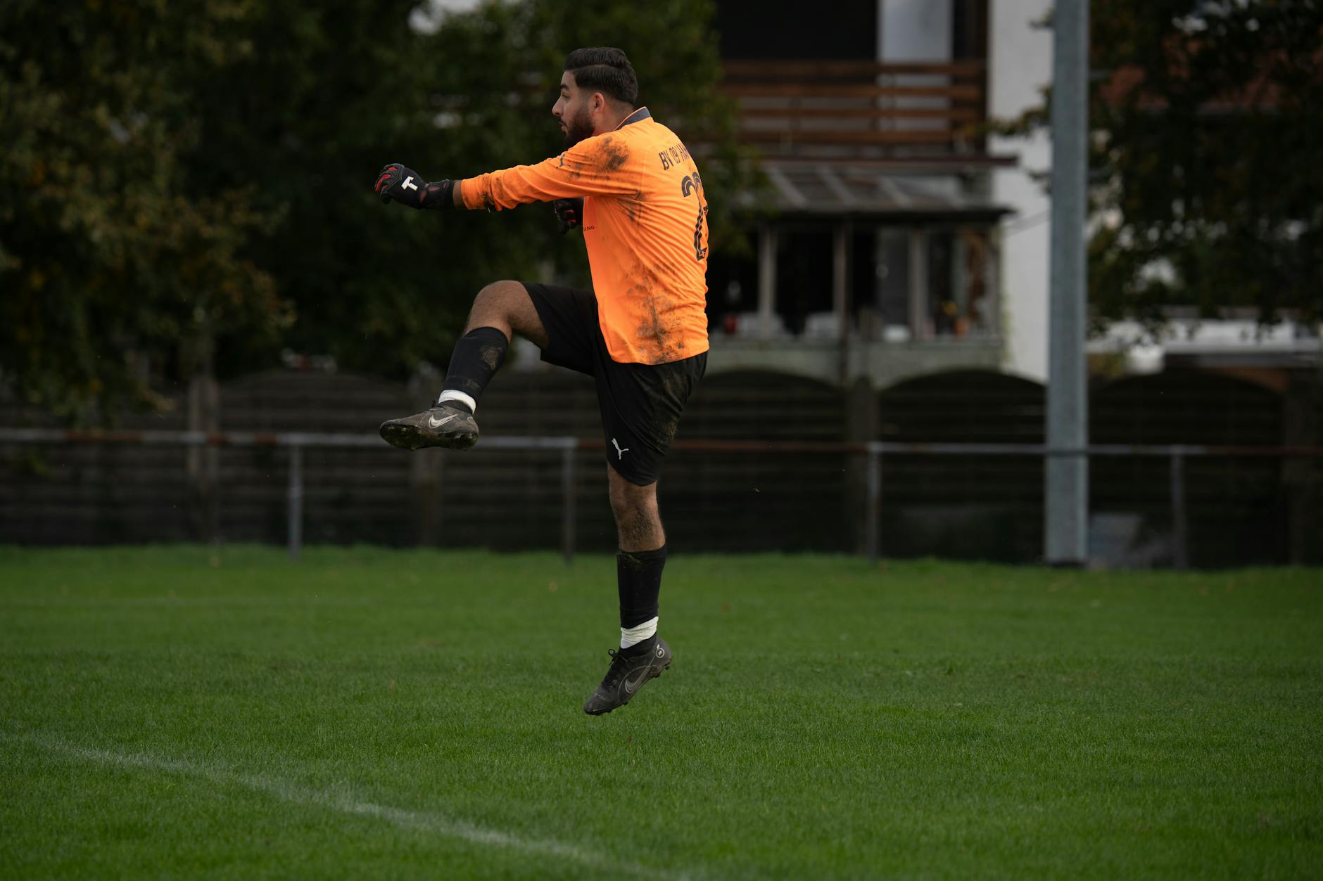 Dynamic shot of a soccer goalkeeper in mid-air kicking action outdoors.