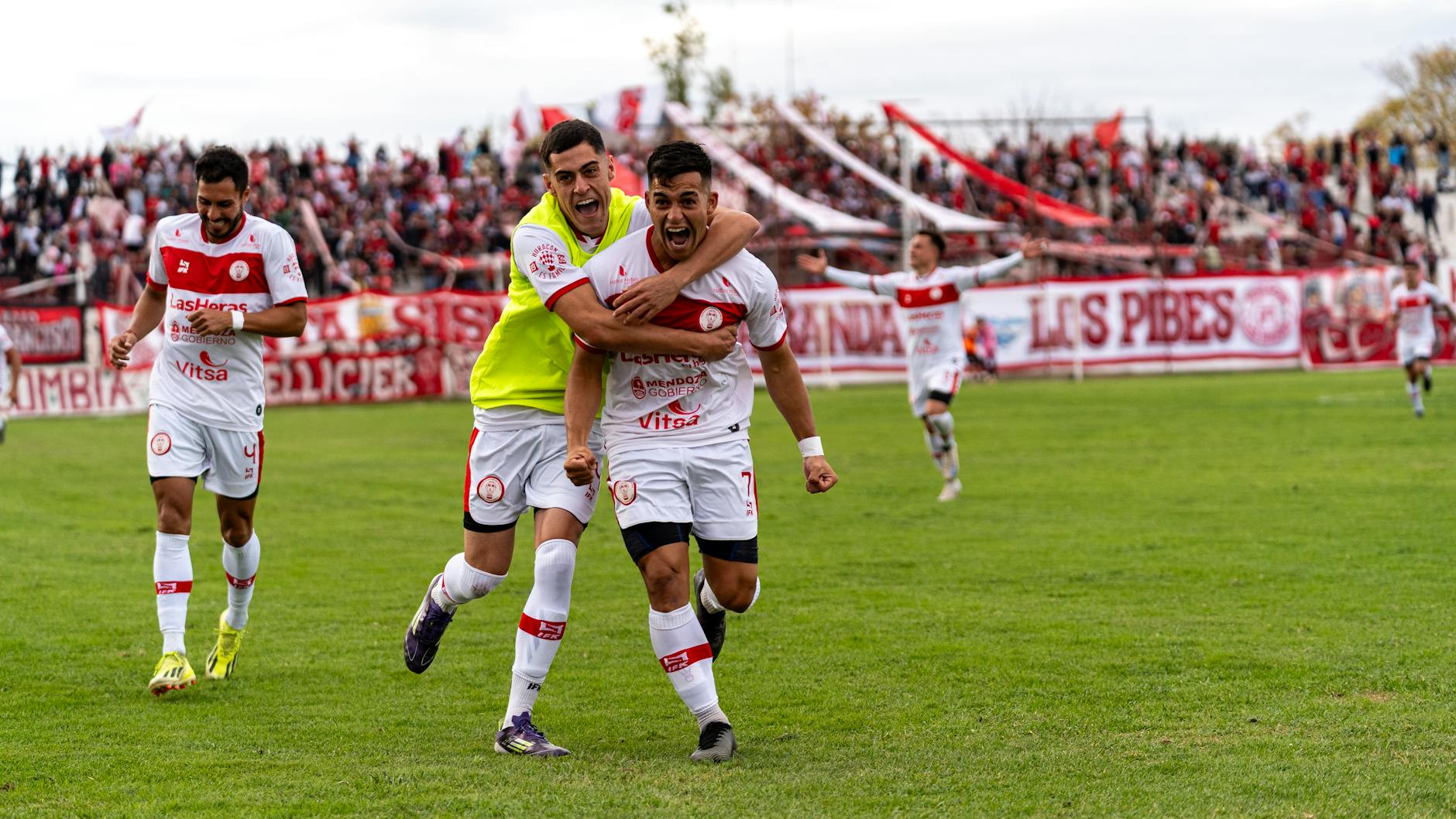 Soccer players celebrating a goal on an outdoor field with cheering crowd.