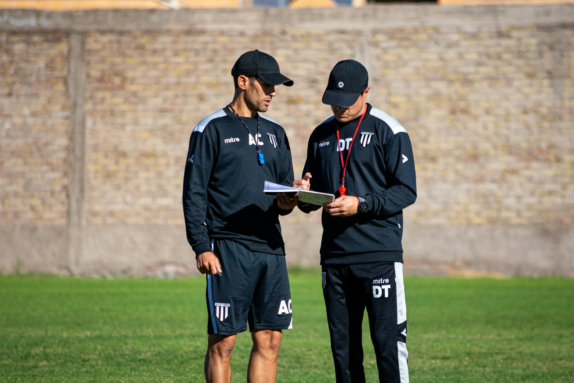 Two soccer coaches reviewing strategies on the field during the day.