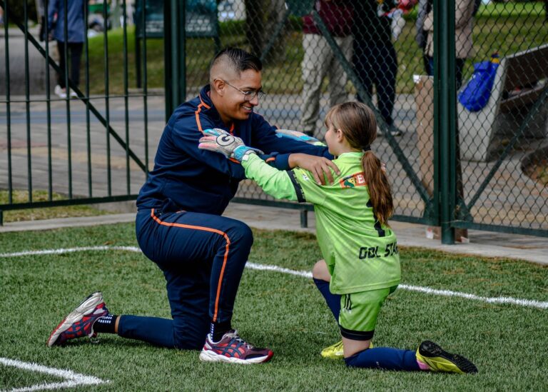 A coach kneels to encourage a young female soccer player in a game.