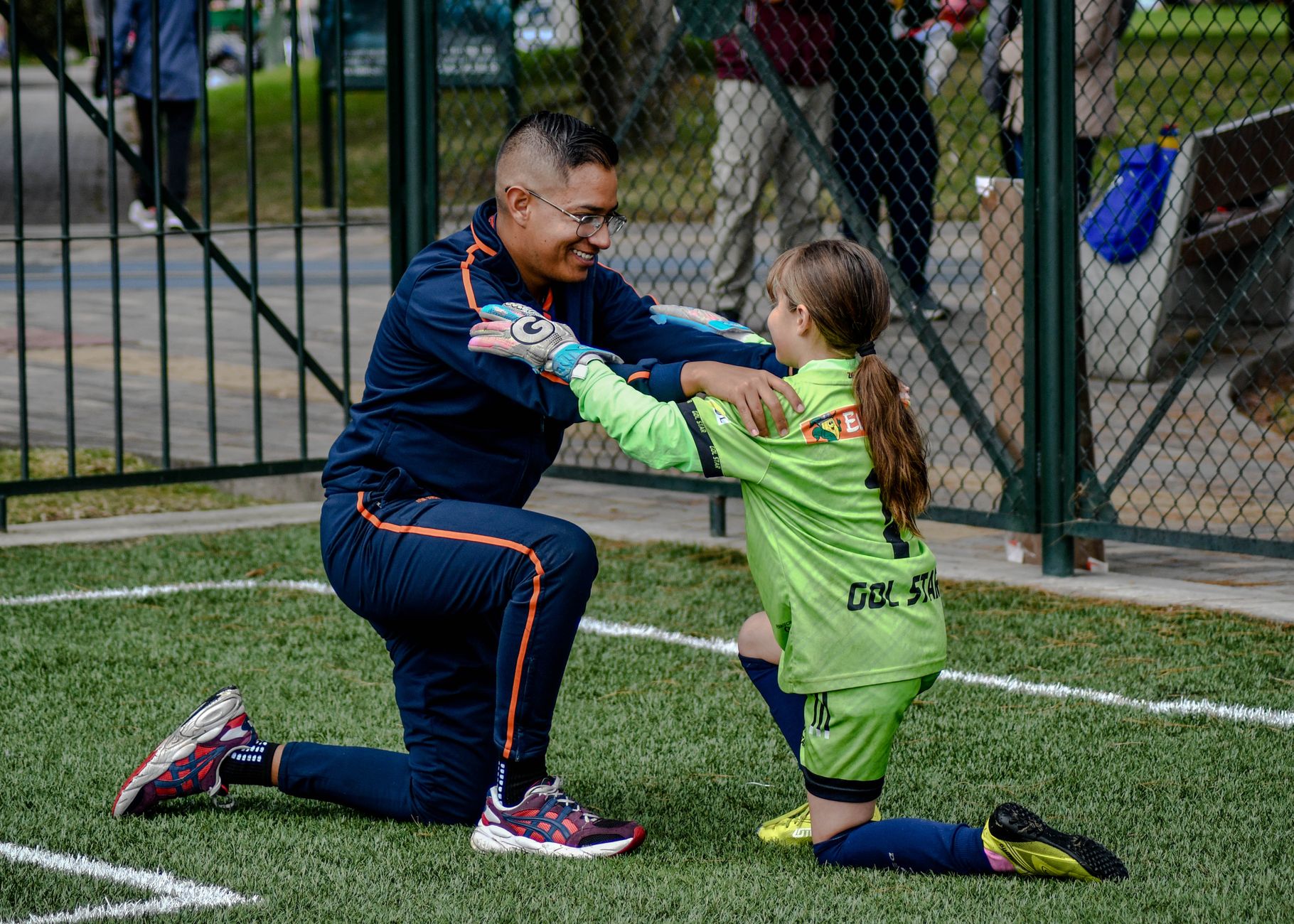 A coach kneels to encourage a young female soccer player in a game.