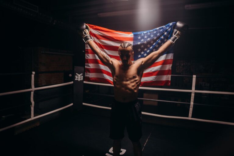 Shirtless boxer triumphs in the ring while holding an American flag, symbolizing victory.