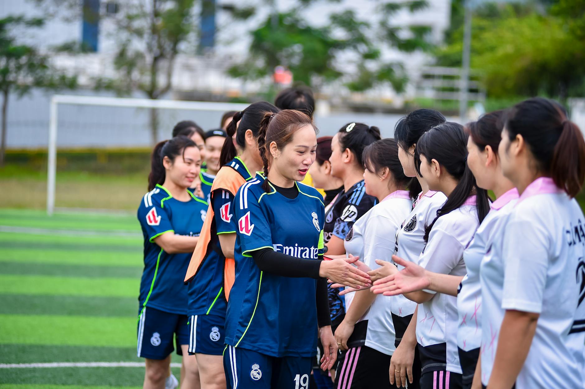 Women's football teams exchanging handshakes on a sports field in Hà Nội, Vietnam.