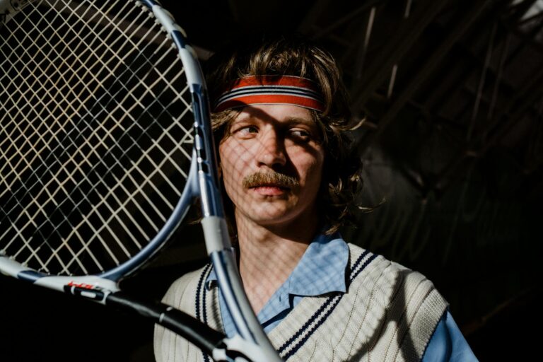 Vintage-style portrait of a man with a mustache holding a tennis racket indoors.