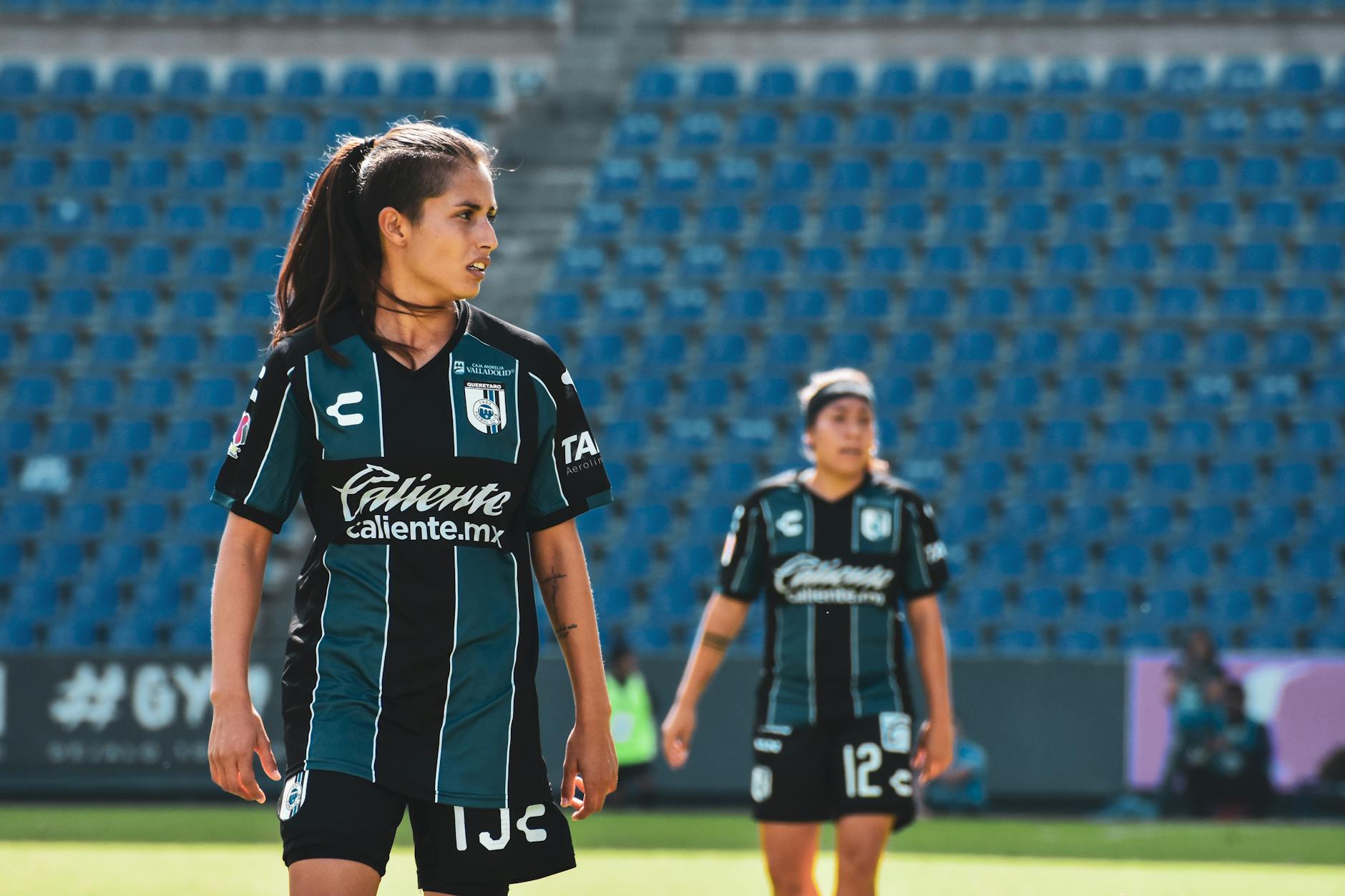 Female soccer players in action during a match at an outdoor stadium in Mexico.
