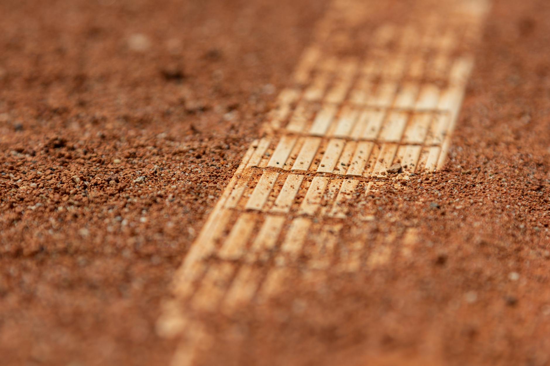 Detailed close-up of a red clay tennis court surface with visible court lines.