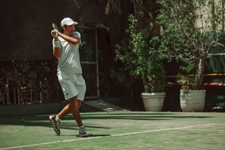 Adult male hitting a tennis ball on outdoor court, sunny weather enhancing action.