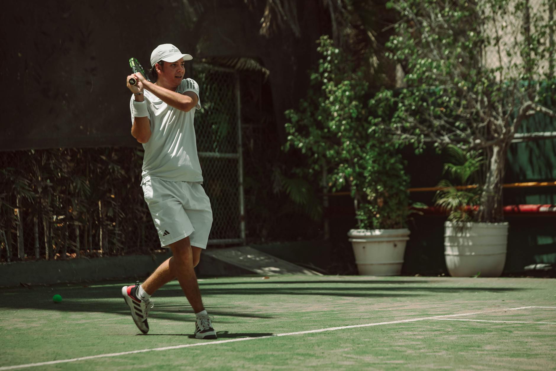 Adult male hitting a tennis ball on outdoor court, sunny weather enhancing action.