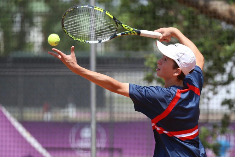 Teenage tennis player in action serving on a sunny outdoor court.