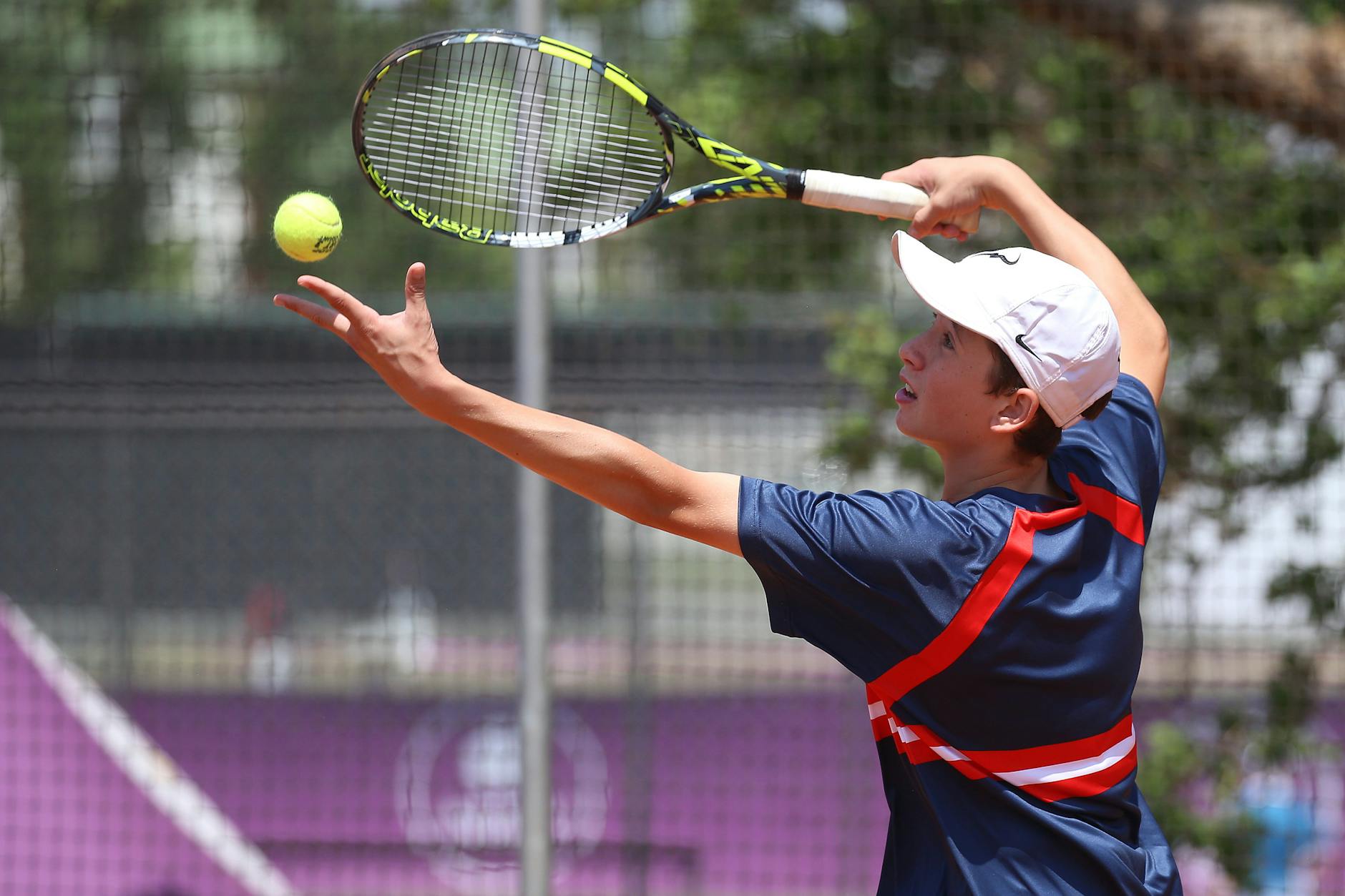 Teenage tennis player in action serving on a sunny outdoor court.