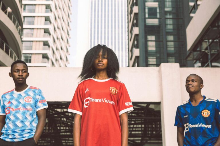 Three young adults in sports jerseys pose confidently in an urban Kenyan setting.