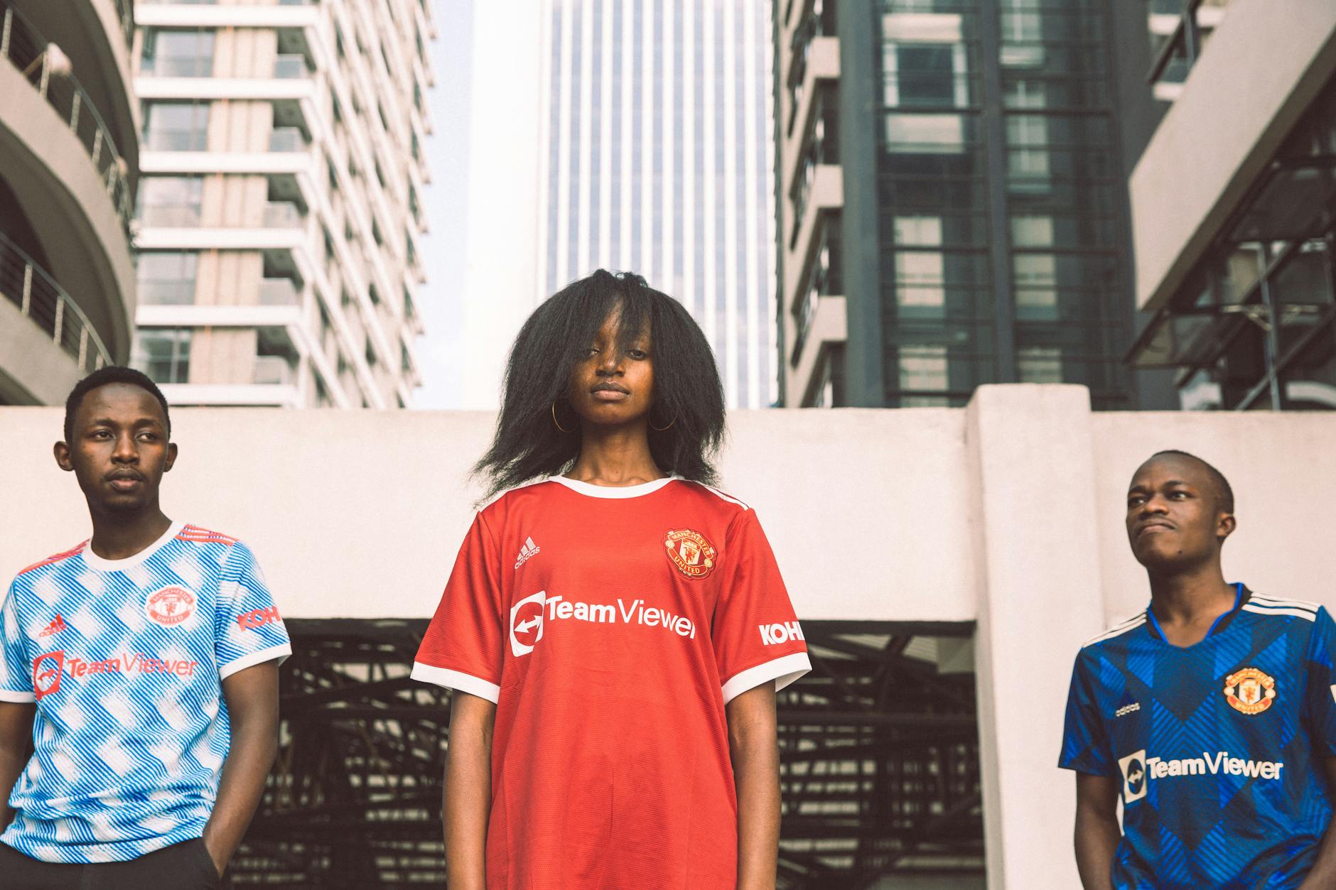 Three young adults in sports jerseys pose confidently in an urban Kenyan setting.
