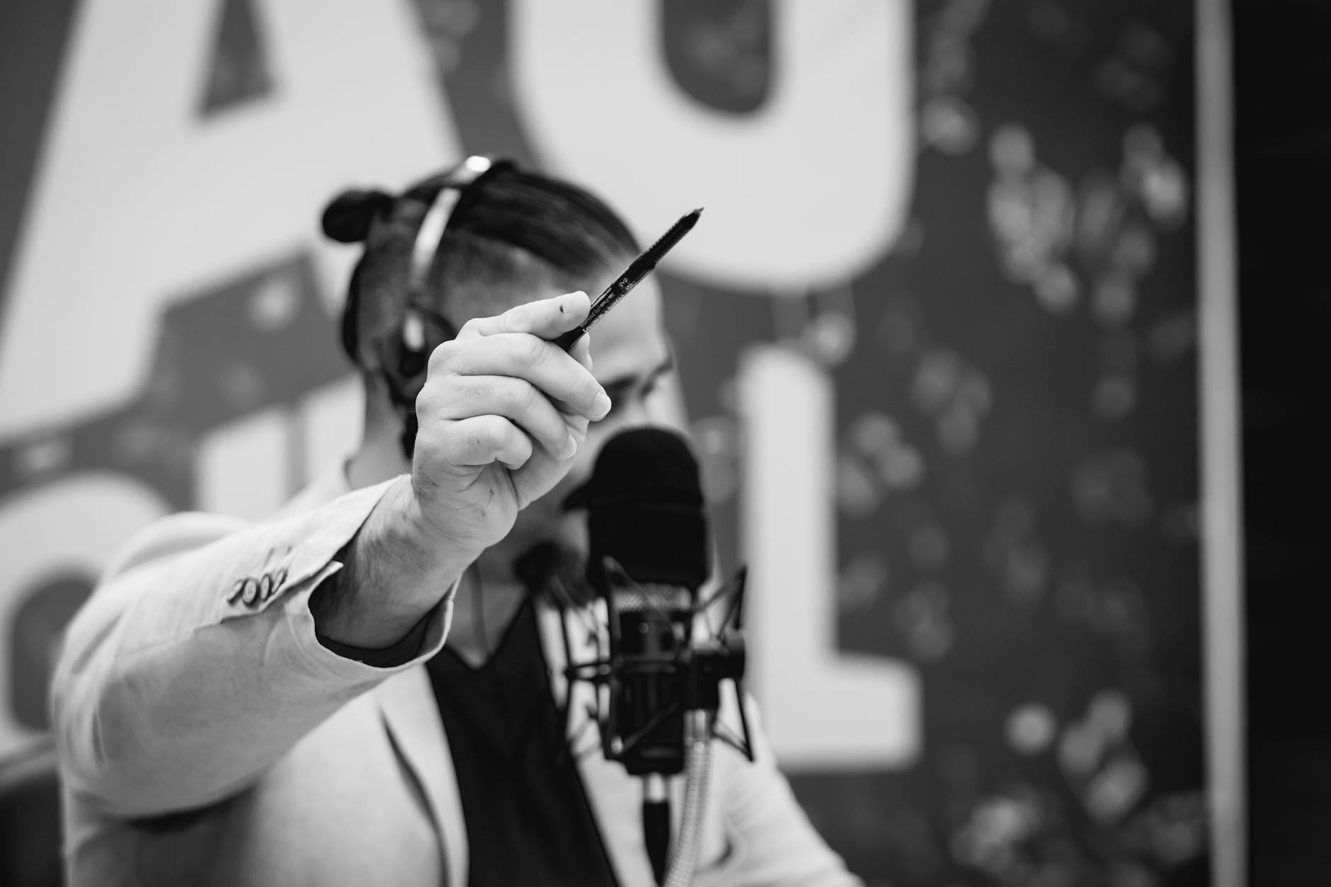 Man engaged in a studio broadcast holding a pen, in black and white.