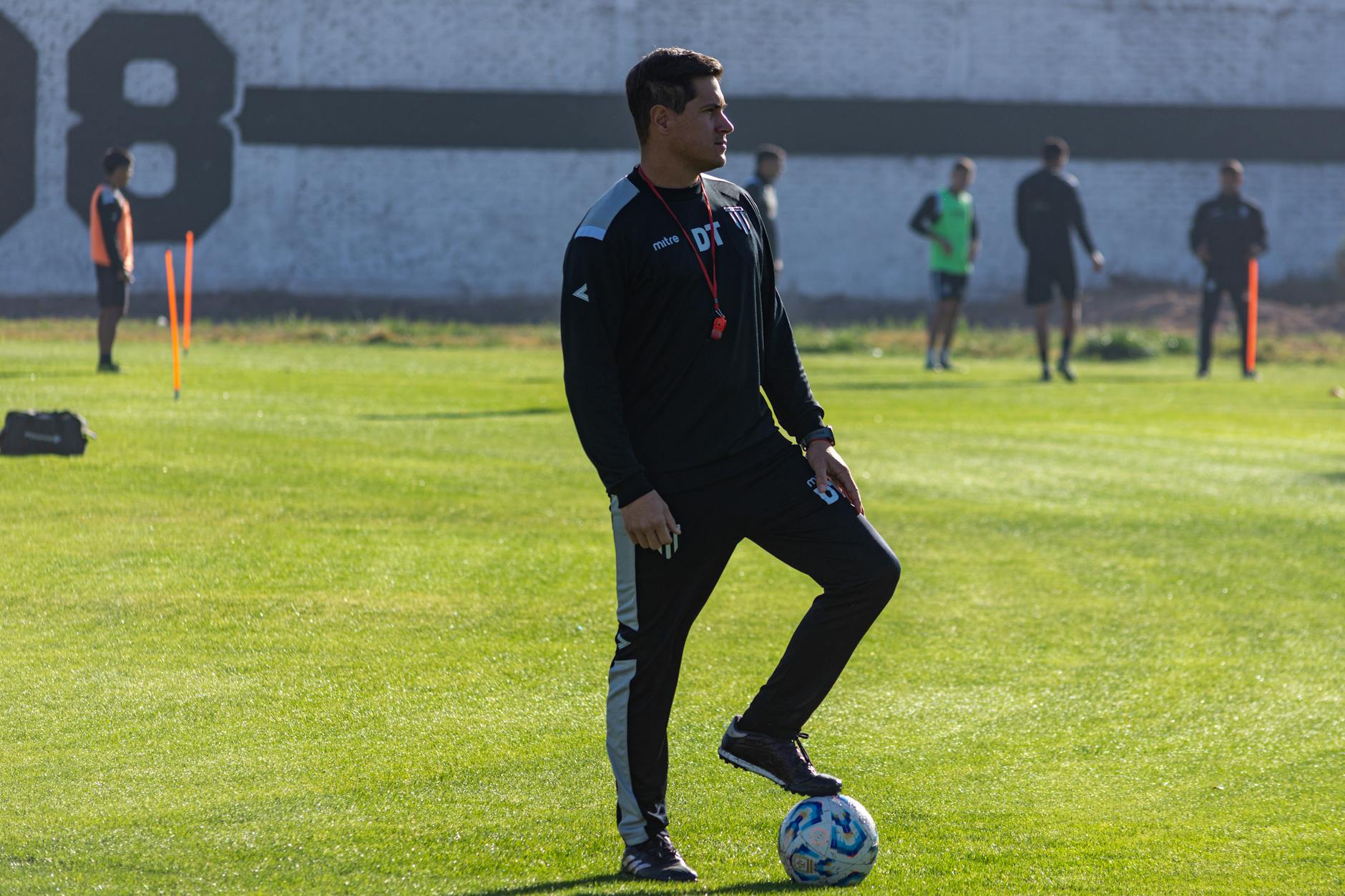 Adult soccer coach guiding players during outdoor training on a sunny day.
