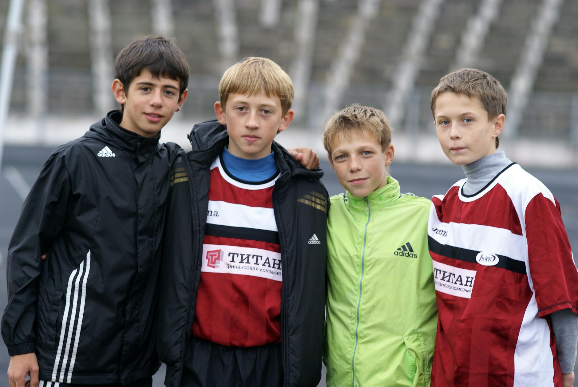 Four young soccer players posing for a team portrait at an outdoor stadium.