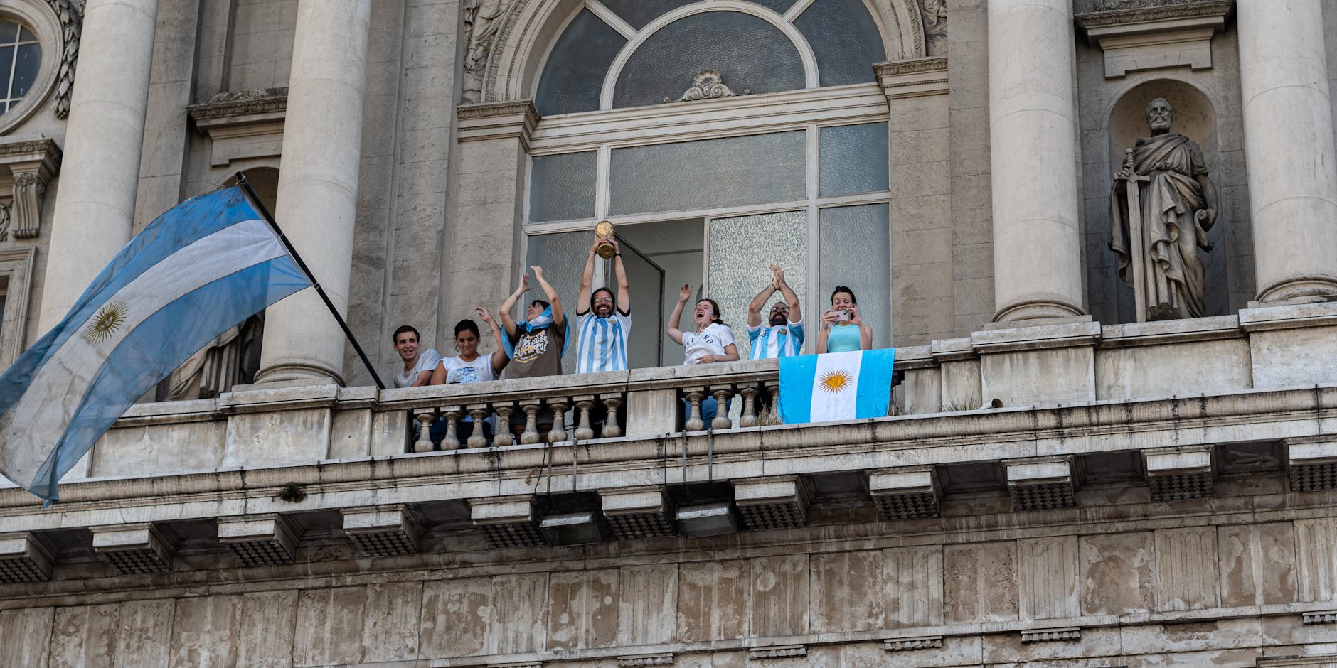 People celebrating with flags and a trophy on a Buenos Aires balcony.