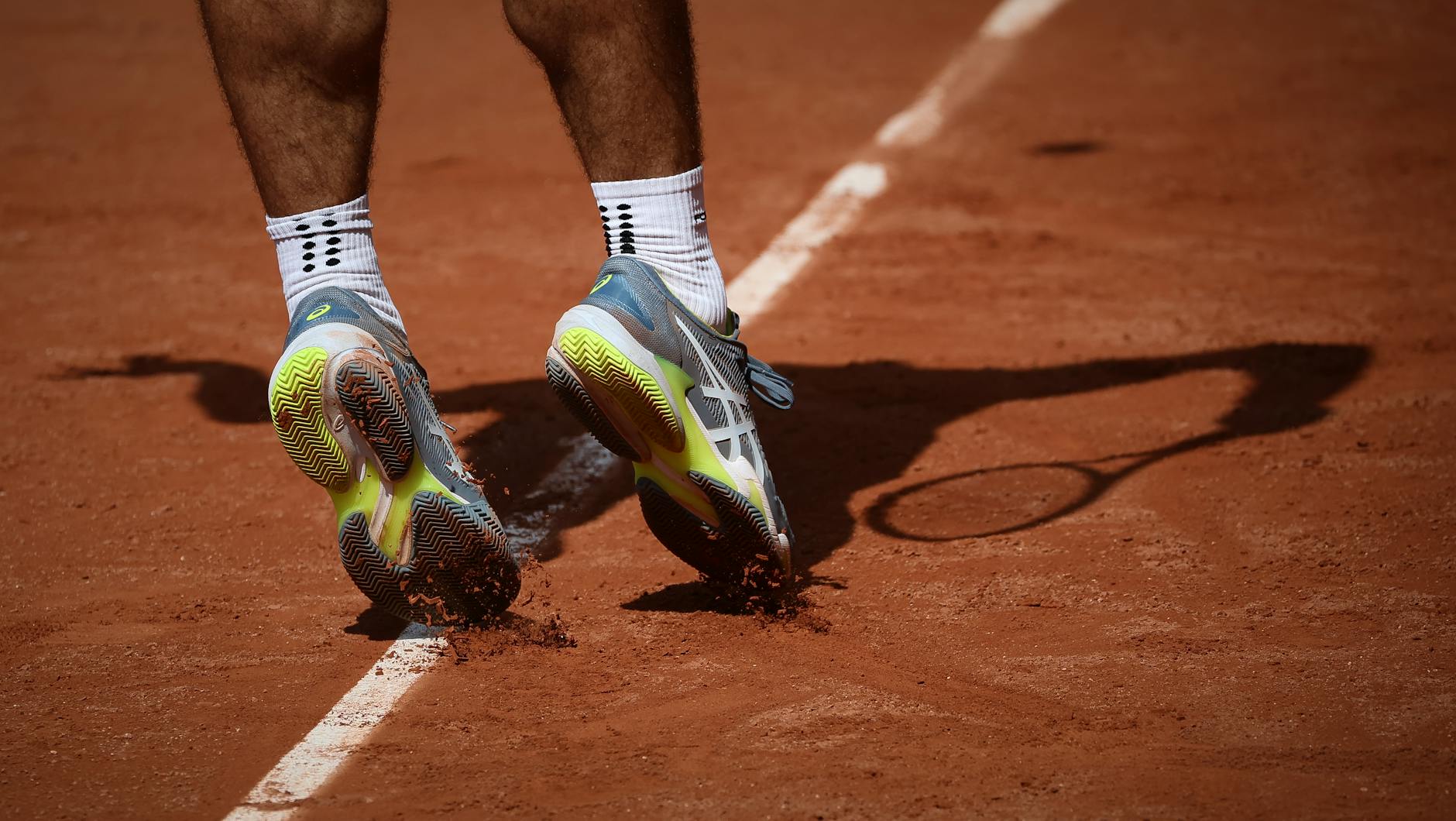 Tennis player in motion on a clay court in Paris, showcasing athletic shoes and dynamic movement.