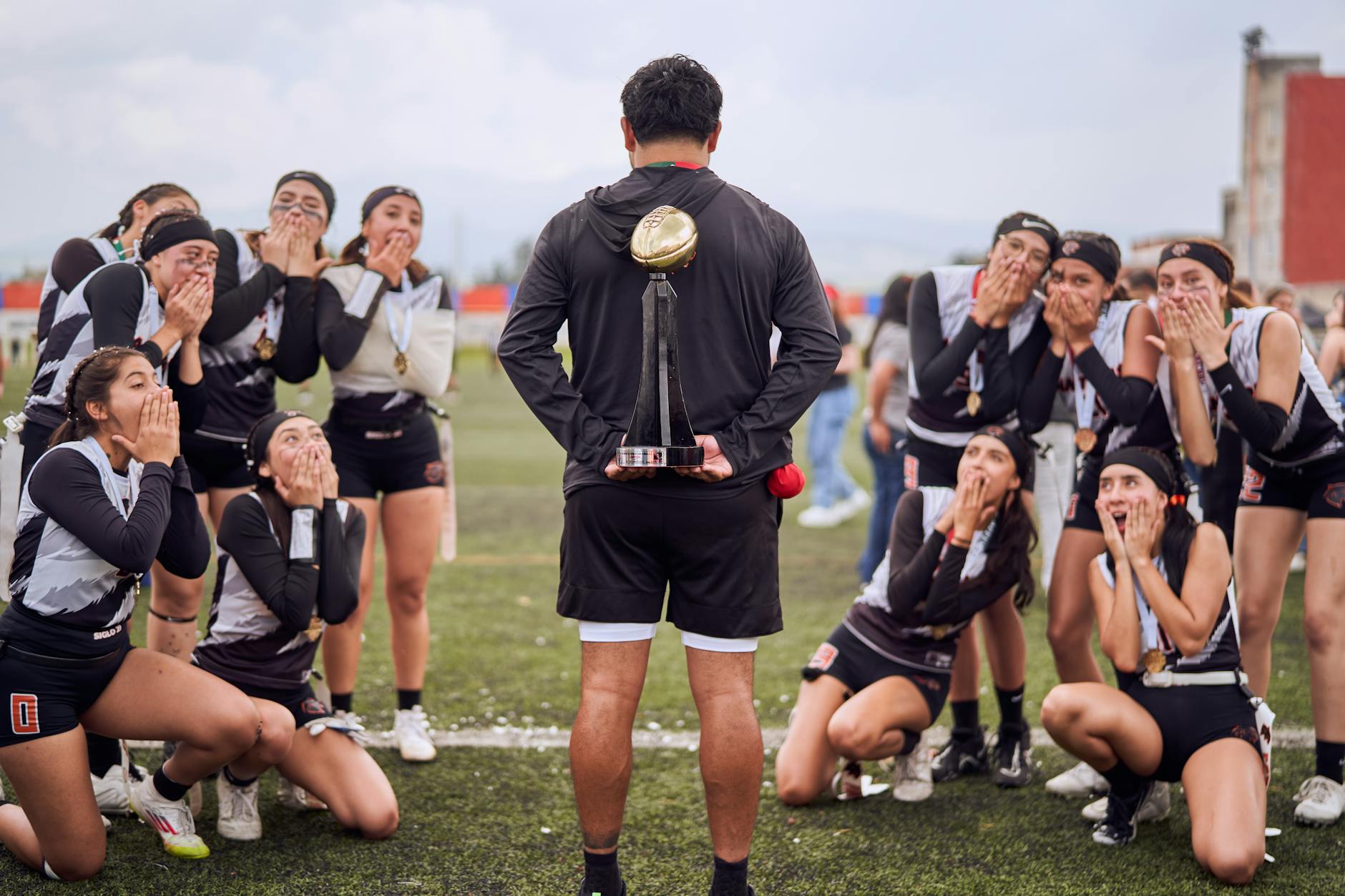 Excited female team celebrating a sports victory with their coach holding a trophy.
