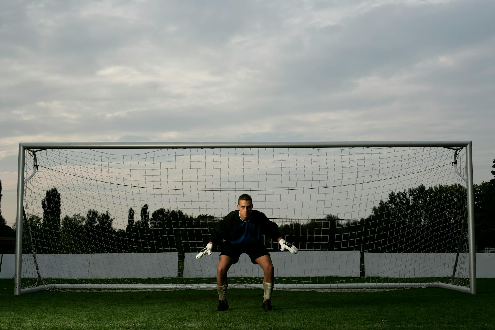 Soccer goalie in action stance ready for defense in front of the net at dusk.