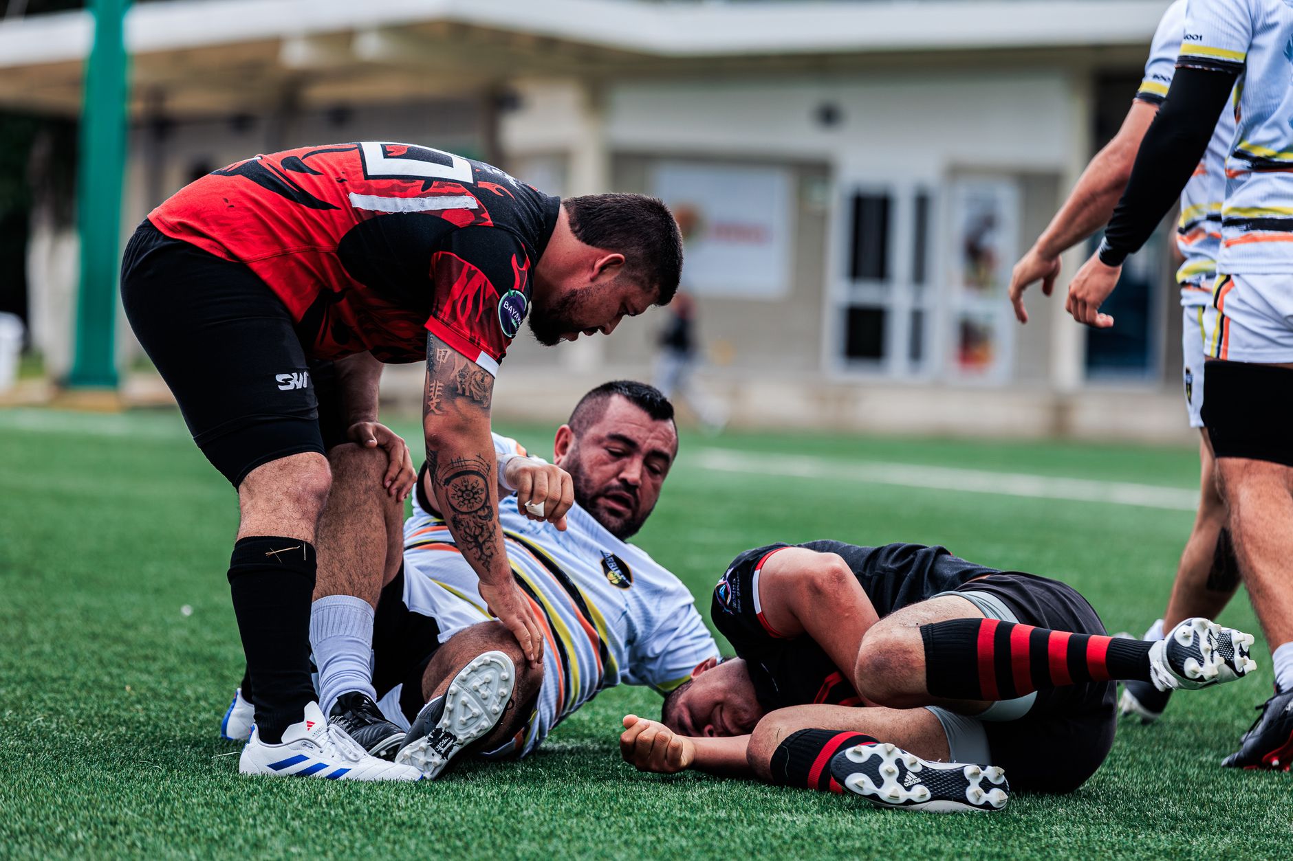 Three male rugby players engaged in a dynamic match on outdoor field.