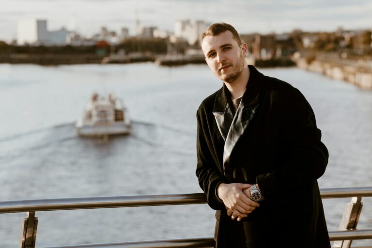 Fashionable man standing on a bridge in Manchester with the cityscape and river behind.