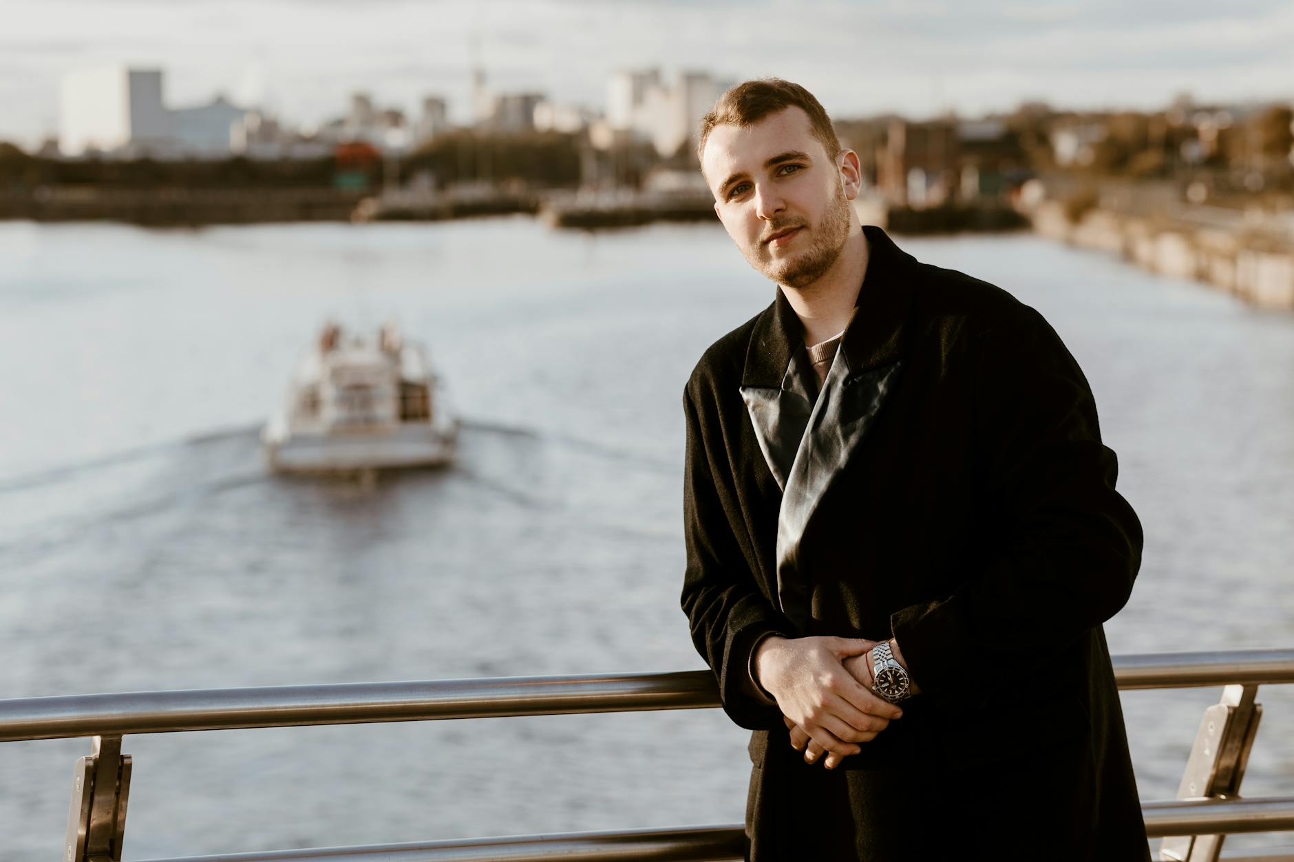 Fashionable man standing on a bridge in Manchester with the cityscape and river behind.