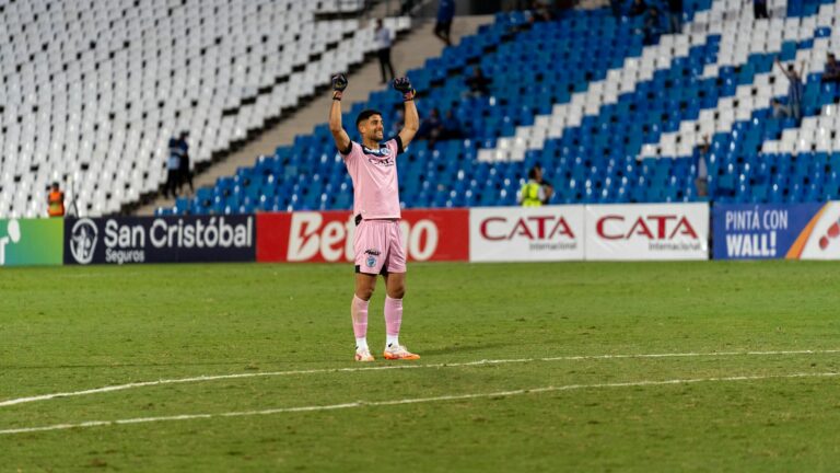 Soccer goalkeeper in pink jersey celebrating victory on the field with raised arms.