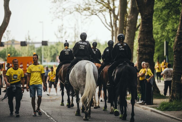 Mounted police patrolling during a soccer match with fans in Borussia Dortmund jerseys.