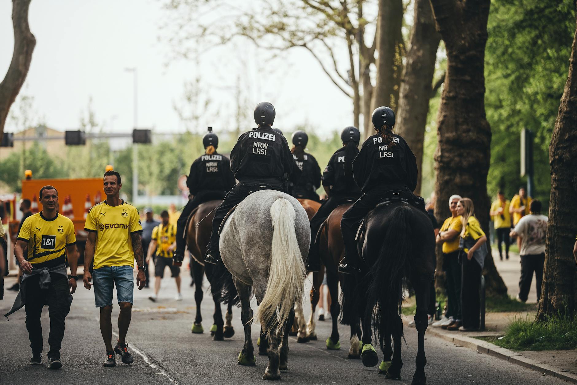 Mounted police patrolling during a soccer match with fans in Borussia Dortmund jerseys.