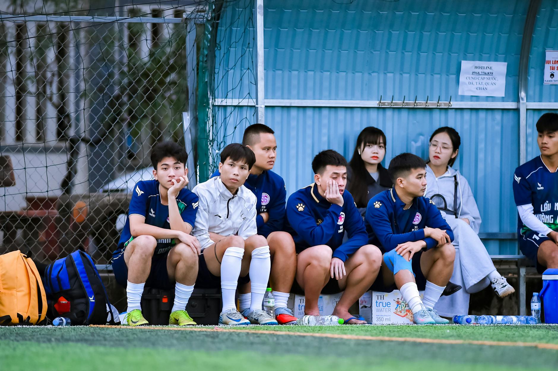 Football players and spectators on a bench during a match in Hanoi, Vietnam.