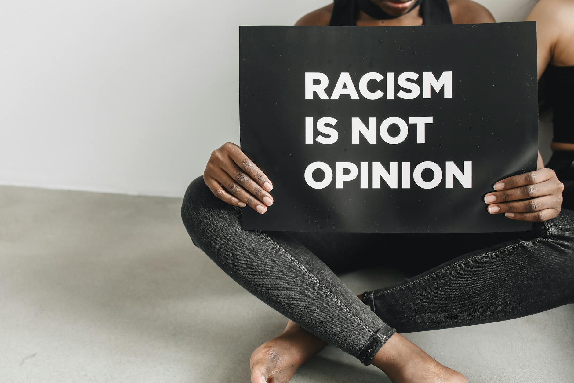 A person holding a 'Racism is Not Opinion' sign indoors, promoting anti-racism.