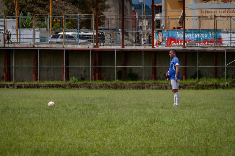 Male soccer player in blue uniform standing on a grassy field in Venezuela.