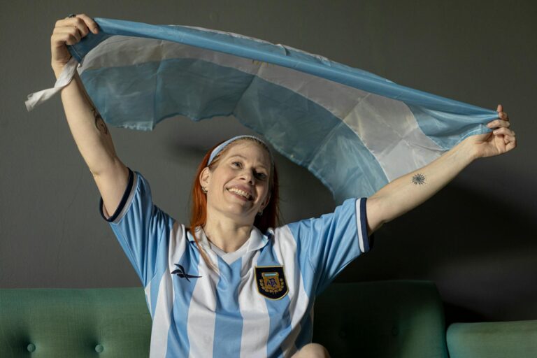A joyful woman holding the Argentine flag indoors, celebrating passionately.