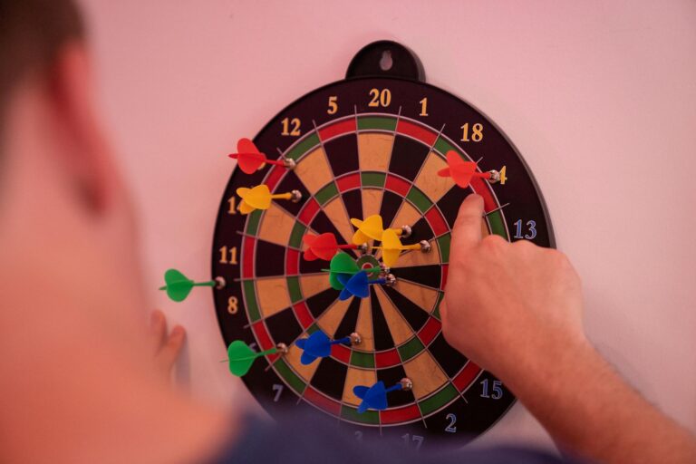 Hand pointing at colorful darts on a dartboard, highlighting accuracy and focus.