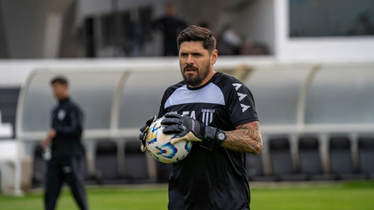 A focused football coach holding a soccer ball on the field during daytime practice.