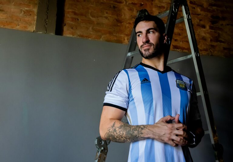 Adult male wearing an Argentina soccer jersey stands confidently indoors.