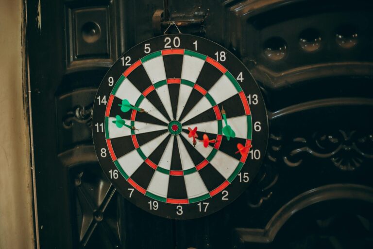 Close-up of a dartboard with red and green darts hitting various spots, indoors setting.